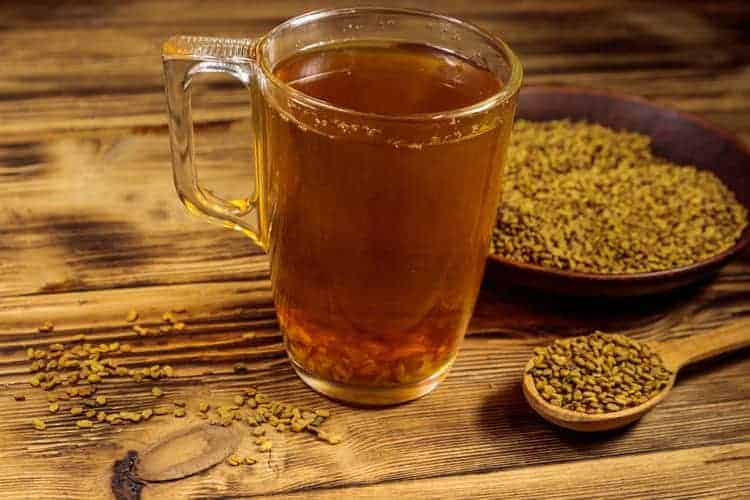 fenugreek tea in a glass surrounded by seeds