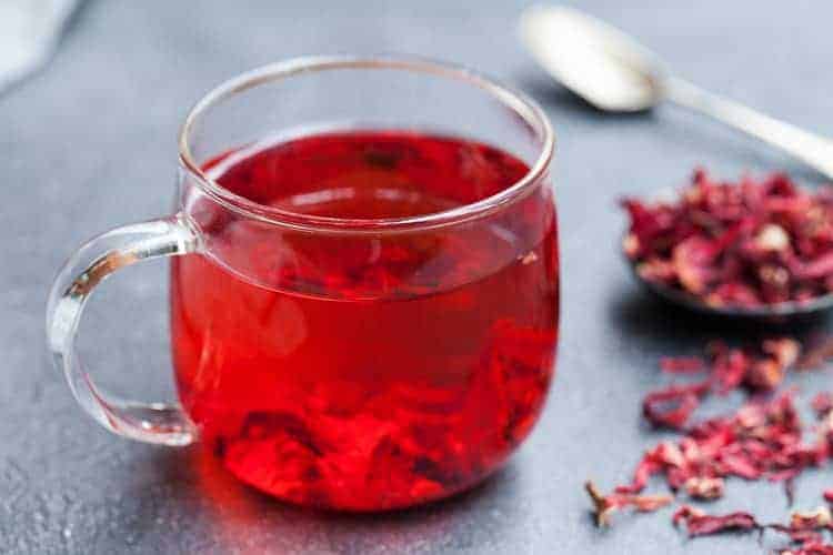 tea rinses for hair growth - hibiscus tea in a glass with hibiscus flowers in the background