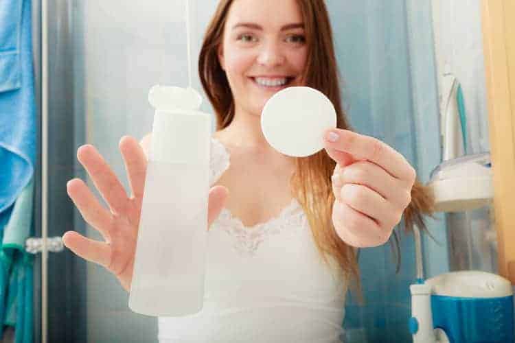 woman holding a cotton pad and cosmetic bottle containing cleansing water