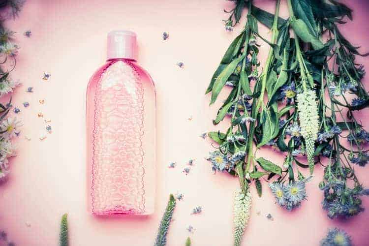 bottle of micellar water with herbs and flowers on a rose background