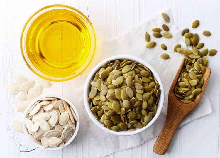 whole pumpkin seeds and oil in bowls