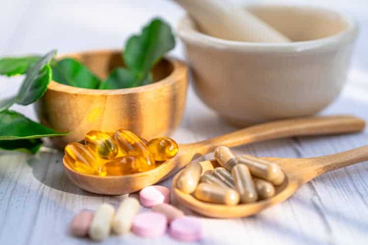 supplement pills in a spoon and herb in a bowl